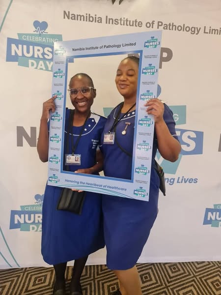 Two PMT nurses holding a Nurses Day frame in front of a Namibia Institute of Pathology backdrop.